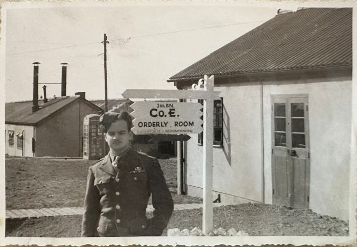 Private Enrique Cisneros Cervantes in WWII uniform beside a Co. E Orderly Room sign